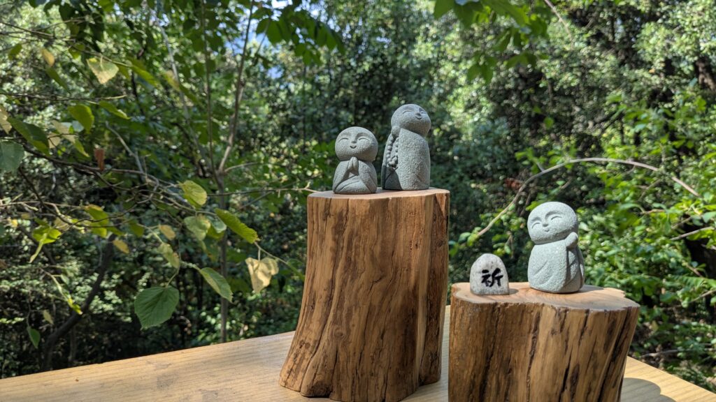 trois statuettes de bouddha japonais jizo en méditation sur des supports en bois dans un décor végétal